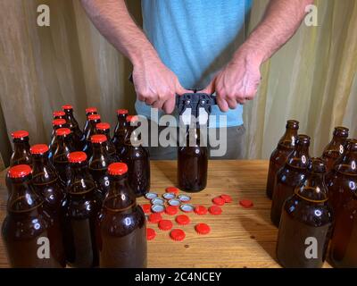 Birra artigianale in casa, l'uomo chiude le bottiglie di birra di vetro marrone con il cappero di plastica su un tavolo di legno con i tappi a corona rossi. Immagine orizzontale di scorta Foto Stock