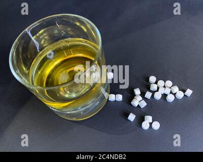 Un bicchiere di whisky con ghiaccio e un sacco di pillole bianche su uno sfondo grigio. Concetto di suicidio con compresse e alcol. Immagine stock. Foto Stock