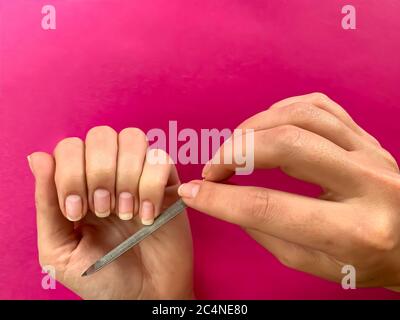 La mano della ragazza della donna limando i chiodi con la lima metallica del chiodo su uno sfondo rosa. Manicure self a casa Foto Stock