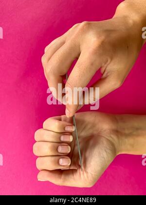 La mano della ragazza della donna limando i chiodi con la lima metallica del chiodo su uno sfondo rosa. Manicure self a casa Foto Stock