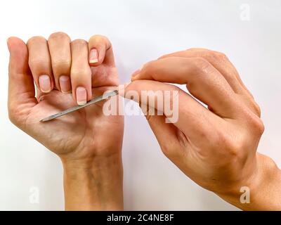 La mano della ragazza della donna limando i chiodi con la lima metallica del chiodo su uno sfondo bianco. Manicure self a casa Foto Stock