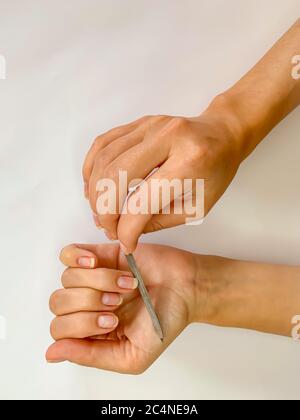 La mano della ragazza della donna limando i chiodi con la lima metallica del chiodo su uno sfondo bianco. Manicure self a casa Foto Stock