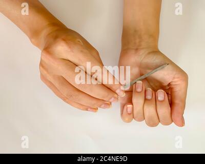 La mano della ragazza della donna limando i chiodi con la lima metallica del chiodo su uno sfondo bianco. Manicure self a casa Foto Stock