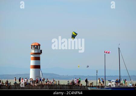 Podersdorf, Austria - 29 aprile 2012: Persone non identificate sul molo con faro e kite surfer sul lago Neusiedler in Burgenland Foto Stock