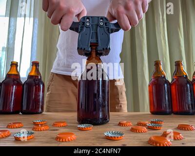 Birra artigianale in casa, l'uomo chiude le bottiglie di birra di vetro marrone con il cappero di plastica su un tavolo di legno con i tappi di corona arancione. Immagine orizzontale Foto Stock