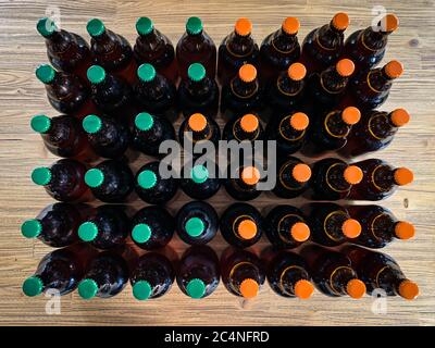 Un sacco di birra fatta in casa propria birreria. Molte bottiglie di birra artigianali in vetro marrone con tappi verdi e arancioni, vista dall'alto piatta su un im orizzontale in legno Foto Stock