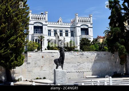 Kavala, Grecia - 13 giugno 2019: Statua della dea Nike di fronte al monumento ai caduti con sollievo e municipio Foto Stock