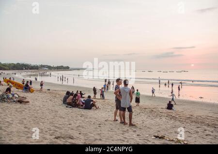 Kuta, Bali, Indonesia - 15 gennaio 2019: I turisti al tramonto si siedono su una popolare spiaggia turistica di Bali. Foto Stock