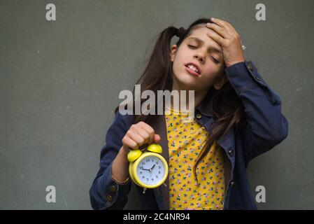 Primo piano di una giovane femmina caucasica che tiene un allarme orologio e sentirsi dimentico Foto Stock