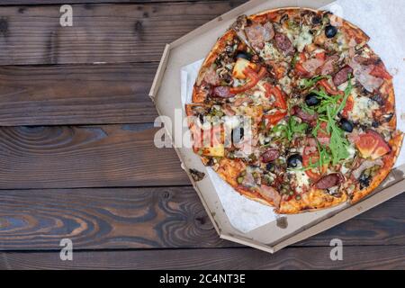 Gustosa pizza con salsicce affumicate Carni pancetta pomodoro rucola formaggio di scatole di cartone per la distribuzione su nero scuro dello sfondo. Copia con spazio per il testo Foto Stock