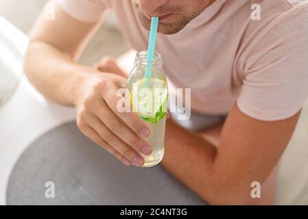 L'uomo beve limonata attraverso una paglia da una bottiglia di vetro. Ritagliato. Foto Stock