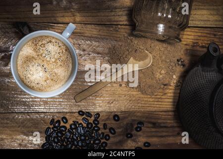 Un primo piano ad alta angolazione di una tazza di caffè a caffè fagioli e terreni e un cucchiaio di legno Foto Stock