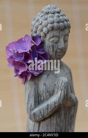 Primo piano di una statua di Buddha con fiori di petalo viola Foto Stock
