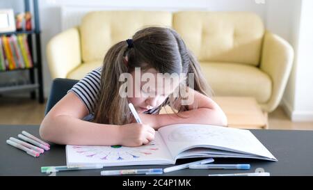 Un bambino sedette a casa e concentrando la colorazione dura in un libro da colorare adulto con penne colorate assortite Foto Stock
