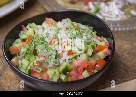 Insalata di verdure fresche israeliane, contenente cetriolo, cipolla bianca di pomodoro e prezzemolo, servita in un recipiente scuro Foto Stock