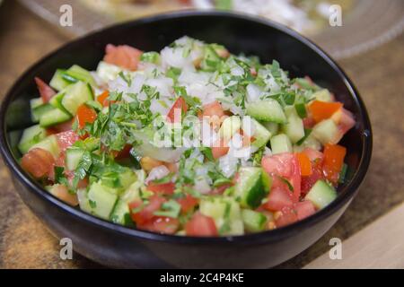 Insalata di verdure fresche israeliane, contenente cetriolo, cipolla bianca di pomodoro e prezzemolo, servita in un recipiente scuro Foto Stock