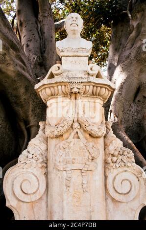 València, Comunidad Valenciana, Spagna. Giardini Glorieta (Jardins de la Glorieta o Jardines de la Glorieta) vicino a Plaza de la porta de la Mar. Monumento dedicato al pittore spagnolo Antonio Muñoz Degrain sotto un albero monumentale Ficus macrophylla. Foto Stock