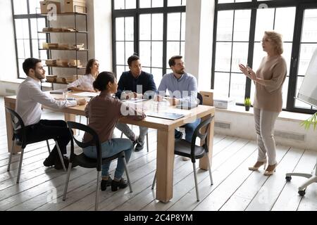 Diversi dipendenti ascoltano la guida di una donna d'affari di mezza età al briefing Foto Stock