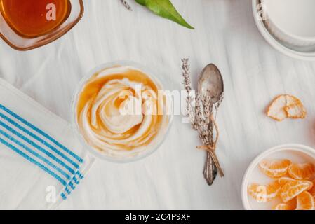 Yogurt greco con dessert al miele. Yogurt con miele, arancia e lavanda. Sfondo bianco e colore blu greco. Sopra la testa. Foto Stock