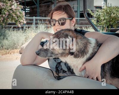 Donna caucasica sta tenendo il suo cane mentre viaggia. Cavalcano in un golf cart elettrico nella natura del nord di Israele il giorno di sole estivo. Misto b Foto Stock