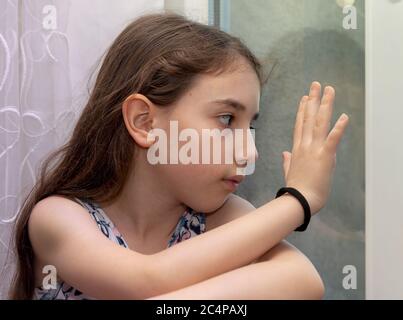 Infelice e annoiata bambina in attesa di dietro la finestra. Una bambina annoiata e depressa ha messo la testa sulle finestre durante la quarantena corona Foto Stock