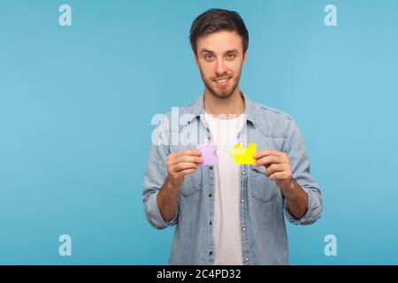 Ritratto di bell'uomo positivo in camicia di jeans lavoratore che tiene due pezzi di puzzle, puzzle colorato, metafora di connessione unità, soluzione completa Foto Stock