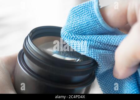 la mano tiene un panno in microfibra per pulire l'obiettivo della fotocamera dslr rimuove la polvere dal vetro dell'obiettivo Foto Stock