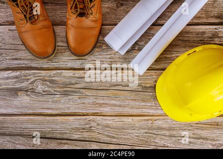 Architetto che lavora con Blueprint Visualizza set di scarpe da lavoro di protezione da lavoro su elmetto giallo in ufficio Foto Stock