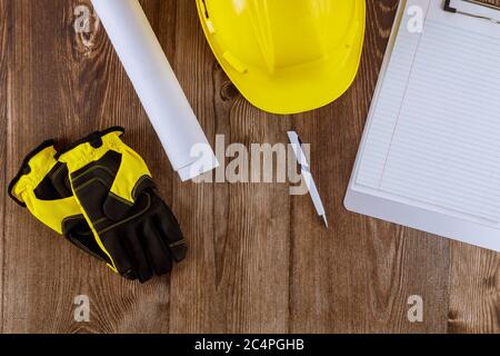 Ingegnere di costruzione ufficio che lavora su rotoli di architettura progetti di casa piani di lavoro giallo casco guanti di protezione su sfondo di legno Foto Stock