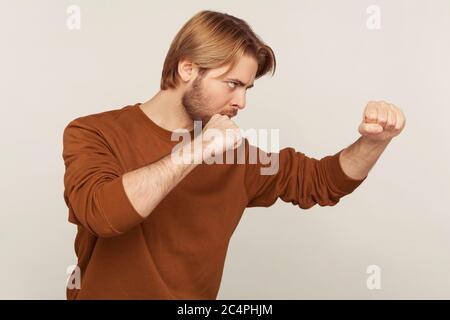 Ti colpisci! Vista laterale di uomo bearded in felpa in piedi con pugni rialzati pugilato gesto, minaccioso di pugno, pronto a lottare, lotta spir Foto Stock