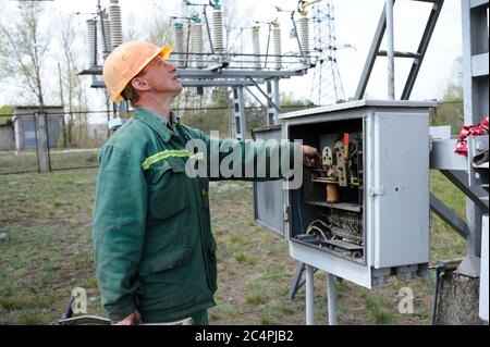 Alla sottostazione elettrica. Operatore che controlla i collegamenti sul quadro elettrico che gira il nottolino di avviamento. Stazione di pompaggio Foto Stock