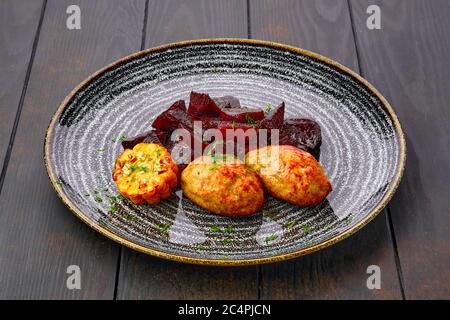 Piatto con cotoletta di maiale fritta con fette di barbabietole arrostite e mais alla griglia su tavolo di legno scuro Foto Stock