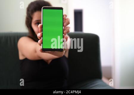 Giovane caucasica che si nasconde dietro lo smartphone con schermo verde. Chiave Chroma. Foto Stock