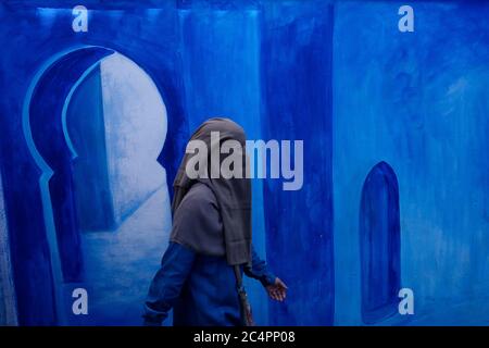 Una donna che indossa un niqab cammina di fronte a un murale decorato blu nell'antica medina. Chefchaouen. Djabala - Regione di Rif. Tanger - Provincia di Tetuan. Nord Foto Stock