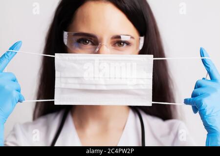 Medico femminile in un cappotto bianco mette una maschera chirurgica sul viso Foto Stock