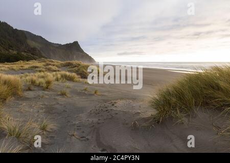 Luce soffusa sulle nuvole e sulla spiaggia, mentre il sole tramonta dietro una nebbia che aggiunge un bagliore dorato alle persone che camminano e Capo Sebastian a distanza Foto Stock