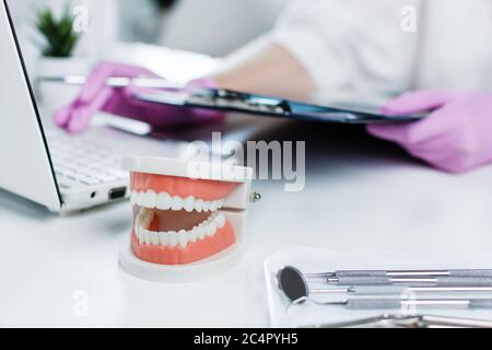 Dentista che tiene la scheda di esame medico del paziente e che utilizza il computer in clinica dentista. Cura dei denti e concetto di trattamento. Assicurazione dentale. Foto Stock