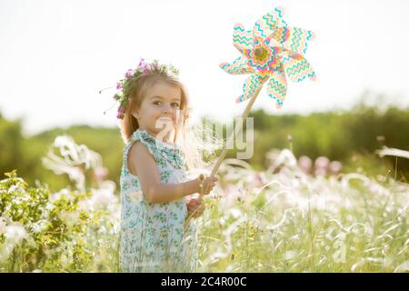 Carina bambina sorridente estate nel campo tenendo un mulino a vento Foto Stock