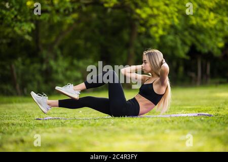 Ragazza sdraiata sull'erba del parco esegue esercizi per rafforzare i muscoli dell'abs. Foto Stock