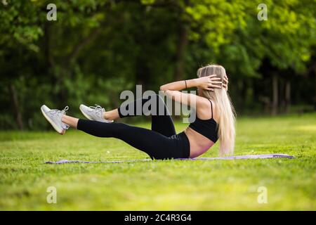 Ragazza sdraiata sull'erba del parco esegue esercizi per rafforzare i muscoli dell'abs. Foto Stock