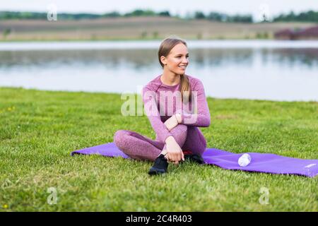 Minato e relax del corpo nel parco. Donna su un tappetino yoga per rilassarsi all'aperto. Giovane donna che riposa sul tappetino dopo l'esercizio Foto Stock