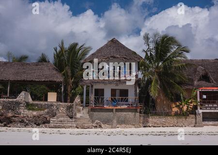 Un albergo sul fronte spiaggia sulla spiaggia di Jambiani a Zanzibar, Tanzania, mentre un uomo fa una passeggiata sulla spiaggia in primo piano Foto Stock