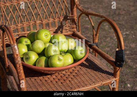Mela verde in un piatto su un tavolo di vimini. Erba verde nel giardino. Tempo di mietitura. Prodotti biologici in stile rustico Foto Stock