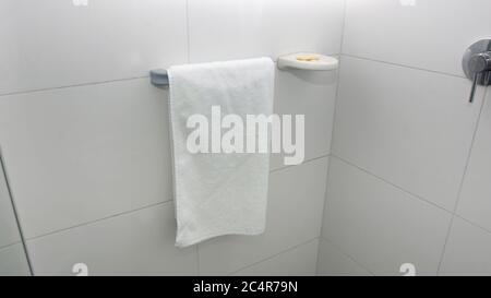 Un asciugamano bianco appeso su un porta-asciugamani in alluminio accanto a un sapone su un porta-sapone con una parete di fondo in ceramica bianca Foto Stock