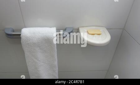Asciugamano bianco appeso su un porta asciugamani in alluminio con una parete di fondo in ceramica bianca Foto Stock