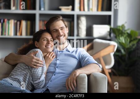 Sorridente giovane coppia sognante che si agguanata, rilassandosi sul divano a casa Foto Stock