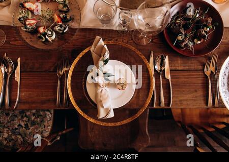 Vista dall'alto del tavolo festivo in legno con piatti, bicchieri e posate. Porzioni di deliziosi piatti esclusivi. Arredamento splendido per feste di nozze. Foto Stock