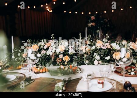 Tavolo da nozze per la celebrazione, servito con piatti, posate e piatti gustosi. Composizione floreale e candele fatte come decorazione. Combinazione elegante di Foto Stock