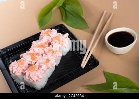 Panini di sushi conditi con formaggio cremoso rosa e gamberi. Panini di sushi in contenitori di plastica neri con salsa di soia e bastoncini di pollo Foto Stock