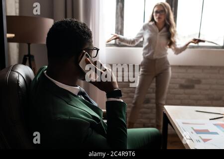 Giovane donna di affari con telefono e bell'uomo africano con portatile in ufficio Foto Stock